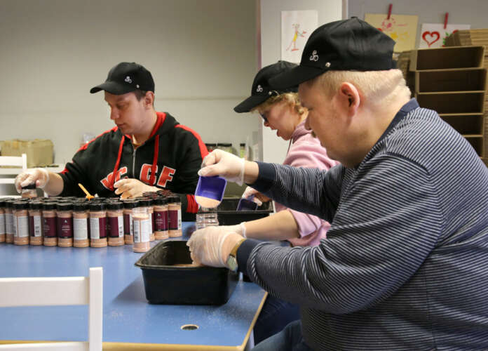 Joona Saarenpää (vas) punnitsee Juhani Laineen ja Reija Toivosen täyttämät maustepurkit. Työskentely sujuu rutiinilla mutta keskittyneesti.