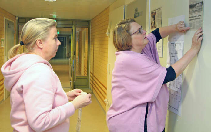 Rehtori Satu Virtanen ja opettaja Anne Mäkelä kiinnittämässä seinään lehtileikkeitä koulun historian varrelta.