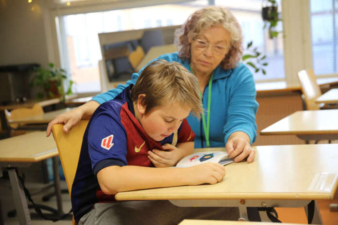 10448005_ Koulumummi Helena Kinnunen kuuntelee, kun toisluokkalainen Miko lukee hänelle ääneen kirjaa. Aikuinen auttaa tarvittaessa ja yhdessä voidaan pohtia tarinan sisältöä.