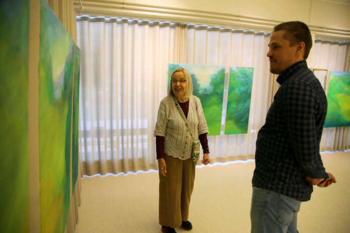 Auran kirjastotoimenjohtaja Sami Lainetoja kuuntelee, kun taidemaalari Anu Tuomi esittelee hänelle Vehreys -näyttelynsä teoksia. Näyttely on esillä Auran kirjastossa heinäkuun ajan.